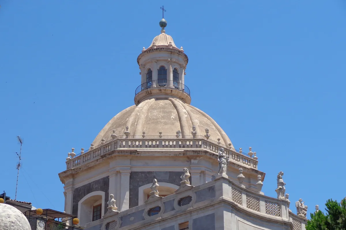 The octagonal dome and lantern of the Badia di Sant'Agata rising above grey stone walls and balustrades under a blue sky.