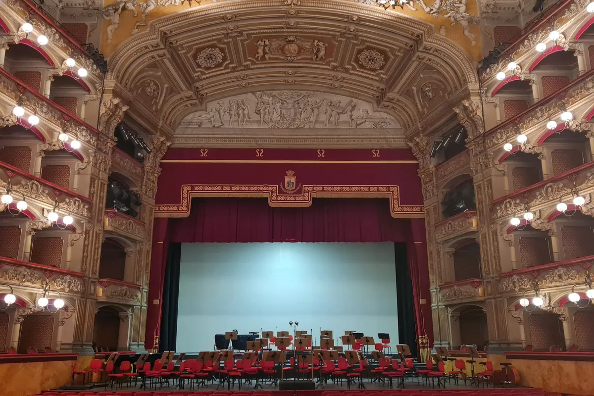 The auditorium of the Teatro Massimo Vincenzo Bellini in Catania, with tiers of boxes lit by globe lamps and a red curtain around the stage